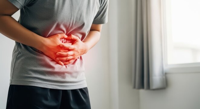 Closeup of a person suffering from severe abdominal pain, stomach ache, or indigestion, holding their stomach with both hands