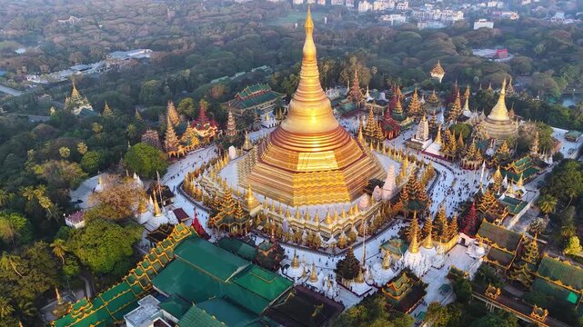 Aerial drone view at Shwedagon Pagoda, a golden stupa, surrounded by lush greenery and urban development in Yangon (Rangun), Myanmar (Burma), showcasing the city's blend of religious and modern life.