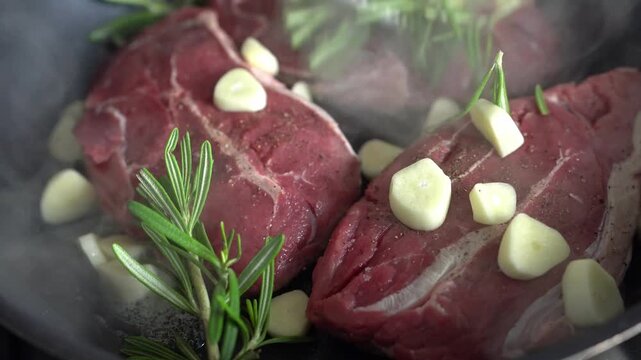 The steaks are cooked in a frying pan with garlic and rosemary. Close-up.