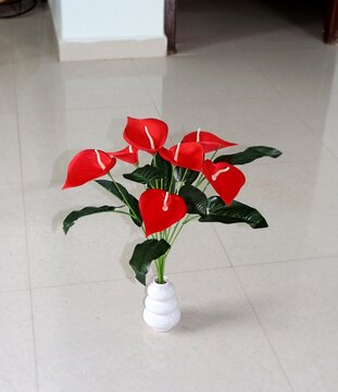 wide petalled beautiful silk-made artificial red flowers with wide green leaves, planted in a decent white ceramic vase. A nice piece for interior decoration.