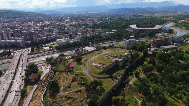 drone view of the historic Skopje Fortress walls running along the hillside next to the Vardar river and city traffic in North Macedonia