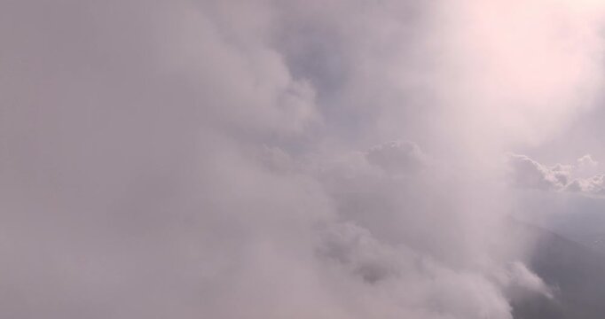 Aerial drone view flying through clouds revealing mountain landscape and valley below with bright sun