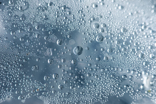 Close up view of wet water droplet and tiny bubble on blue glass surface showing condensation from heavy rain, evoking calm, serene and peaceful mood