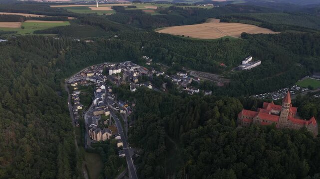 Magnificent aerial footage showing the picturesque town of clervaux and the historic saint maurice abbey, both nestled among the lush green hills and dense forests of the luxembourg ardennes