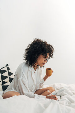 Woman journaling in bed enjoying morning coffee self-care routine