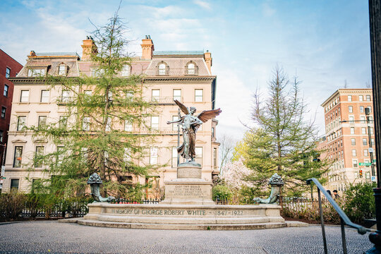 Historic angel monument in urban park before grand mansion facade