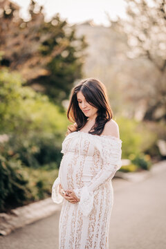 Pregnant woman embracing belly in white lace dress outdoors
