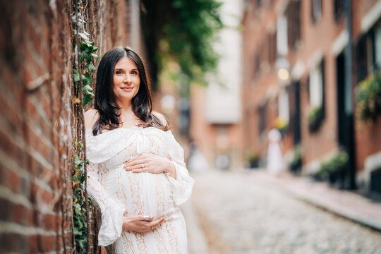 Pregnant woman in lace dress posing in historic cobblestone alley