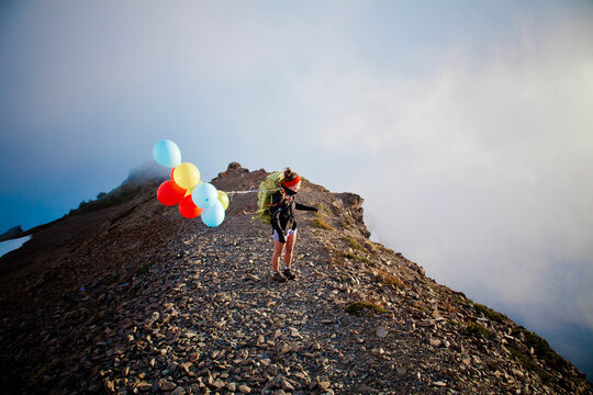 Young woman hiking a rocky ridge with balloons