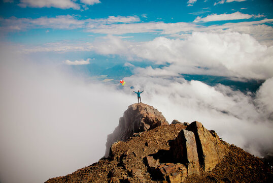 Woman with balloons stands on a mountain summit above the clouds