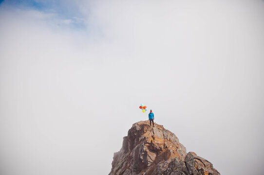 Person holding colorful balloons on a mountain summit