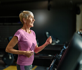 Naklejka premium Portrait of a senior elderly woman exercising in a gym, running using threadmill machine equipment, healthy lifestyle and cardio exercise at fitness club concepts, vitality and active senior
