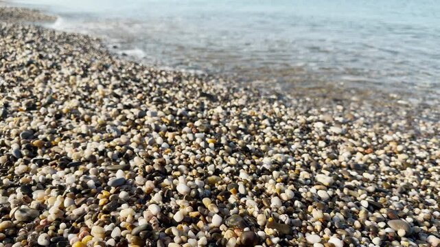 Small waves roll across the calm sea and glide onto the shore. The moving water flows through the smooth pebbles, creating a gentle splashing and soft rattling sound.