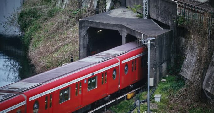 Red, Japanese train passing through tunnel in hill - high shot