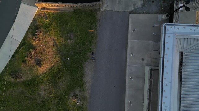 man flying drone looking down rising at dusk in small urban area next to road and train track grass field hobby looking up birds eye view aerial