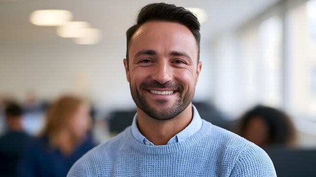 A smiling professional man in a blue shirt works in a bright modern office setting