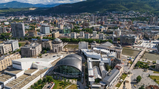 Wide aerial view of Skopje city center featuring modern and neoclassical architecture, the Vardar river, bridges, and mountain ranges in North Macedonia