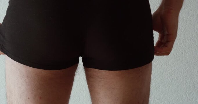 Close-up shot of a man adjusting uncomfortable boxer briefs that ride up, showing clothing discomfort, underwear fit problems, irritation, chafing, and everyday personal inconvenience.