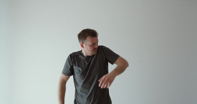 Wide shot of a man reacting to severe shoulder pain and attempting to move an injured arm, representing shoulder dislocation, emergency pain, physical trauma, and musculoskeletal problem