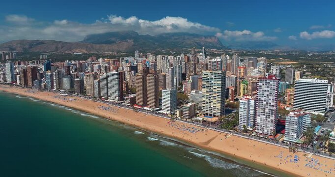 Benidorm beachfront aerial summer Spain skyscrapers Levante beach dramatic clouds mountain backdrop Mediterranean coastline Alicante tourism resort slow motion drone wide panorama skyline