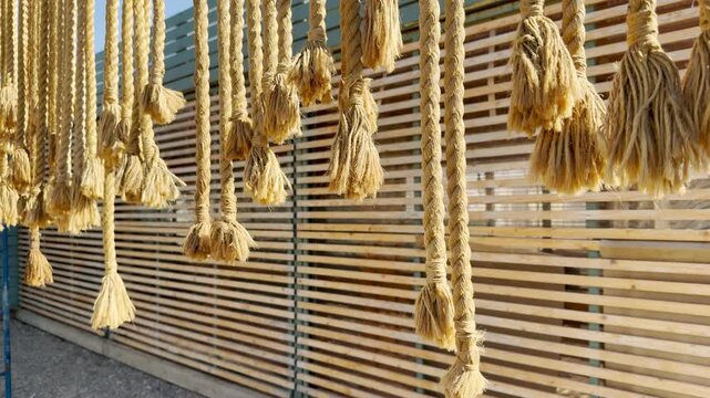 Thick, rustic ropes with frayed ends dangle playfully in the warm sunlight. Their natural textures create a cozy, serene mood against a slatted wood backdrop.