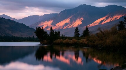 Warm sunset colors reflect stunning mountain ranges in a calm body of water creating a tranquil and breathtaking landscape scene © Thares2020