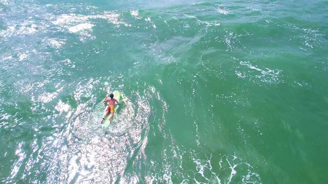 4K aerial shot of a man surfing and enjoying sunbathing on the sea