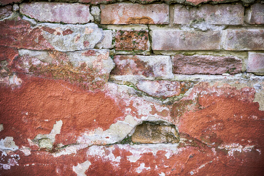 Decaying red wall with broken plaster close up