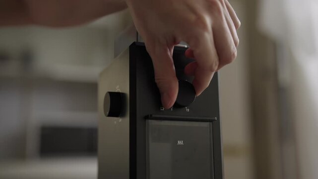 Close-up of person hand adjusting settings on modern electric coffee grinder, turning dial to select desired coarseness for brewing perfect cup of coffee. Shooting in slow motion