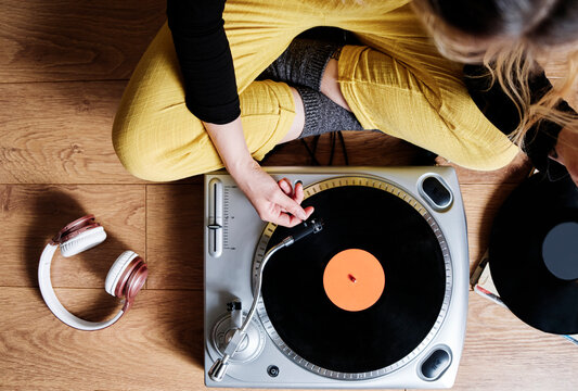 Woman adjusting tonearm of turntable while sitting on floor at home