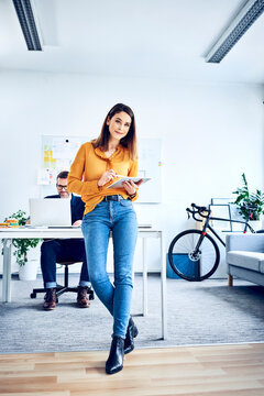 Portrait of businesswoman using tablet in office with colleague in background