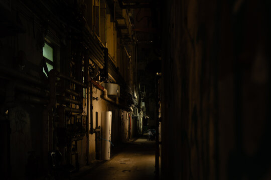 A narrow service alley between building backs in Wan Chai, Hong Kong Island, at night, with dense exposed pipework, ducting, and utility infrastructure lining the left wall.