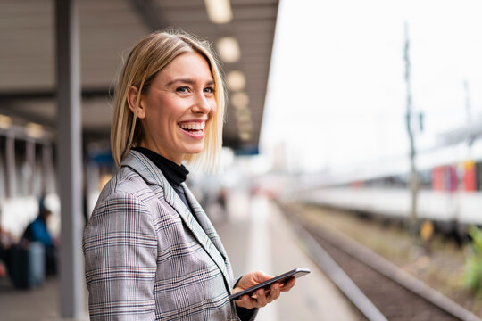 Happy young businesswoman with mobile phone at the train station