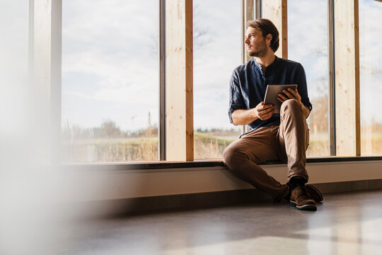 Businessman with tablet looking out of window in open-plan office
