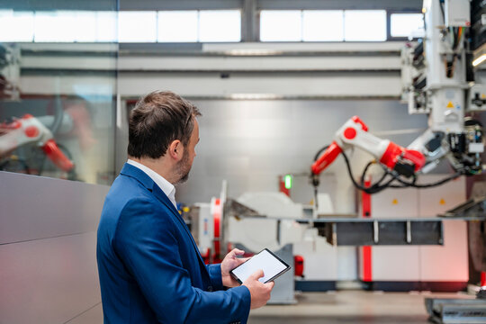 Manager using tablet to control industrial robot in factory