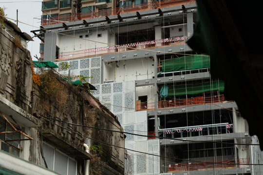 An aged low-rise building with weathered concrete and overgrown vegetation sits directly in front of a large construction site in Yau Ma Tei, Kowloon, Hong Kong.