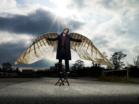 Dreamer with large wings standing on a chair outdoors