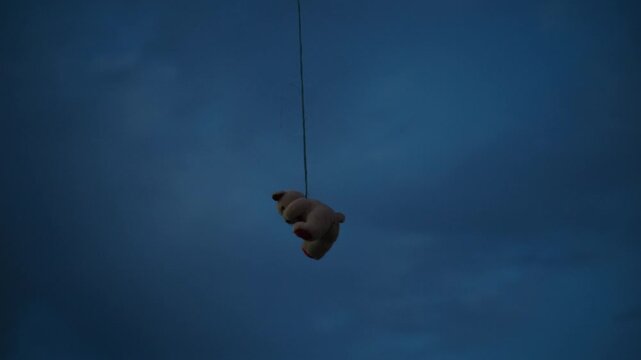 Stuffed bear toy suspended high in the air with large copy space. Surreal image representing isolation, vulnerability, memories and mental health themes. 4K.