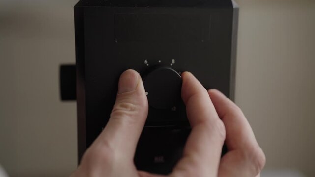 Person adjusting grind size setting on black electric coffee grinder for preparing espresso, close-up shot concept of dial being turned to finer setting for optimal brewing. Shooting in slow motion