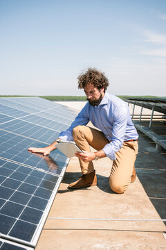 Businessman inspecting solar panels on roof with tablet and smiling