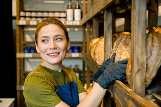 Salesperson working in bakery holding freshly baked bread on shelf