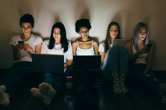 Group of female friends at home sitting on floor using technology in the dark