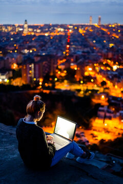Young woman sitting on railing above the city using cell phone, Barcelona, Spain