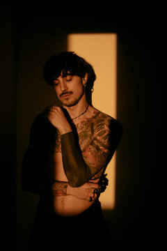 Sensual portrait og young man with tattoo in dramatic warm indoor lighting