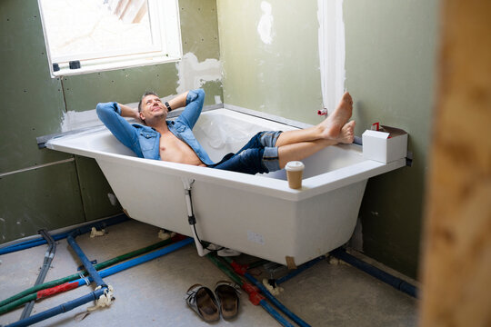 Smiling man with hands behind head lying in bathtub in attic