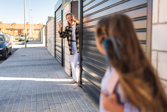 Mother waving at daughter returning home from school