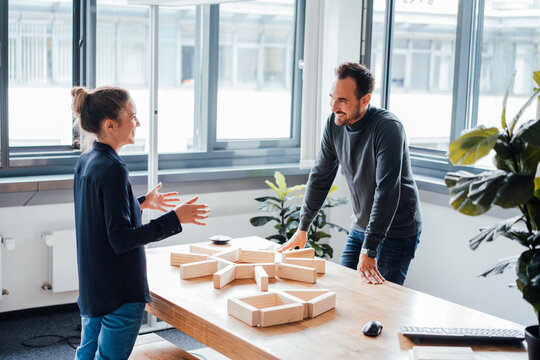 Happy business colleagues discussing over wooden blocks in office