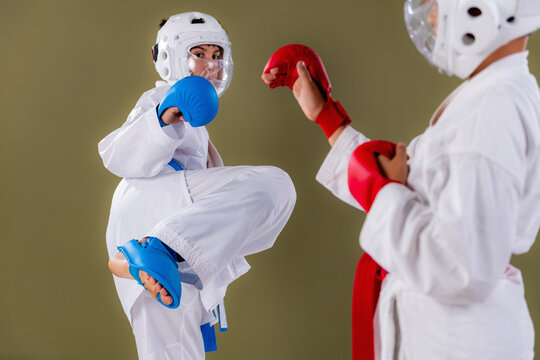 Karate athlete raises knee high in preparation for a kick while opponent holds a defensive guard, capturing the chambering phase of a lower body striking technique during a competitive sparring drill.