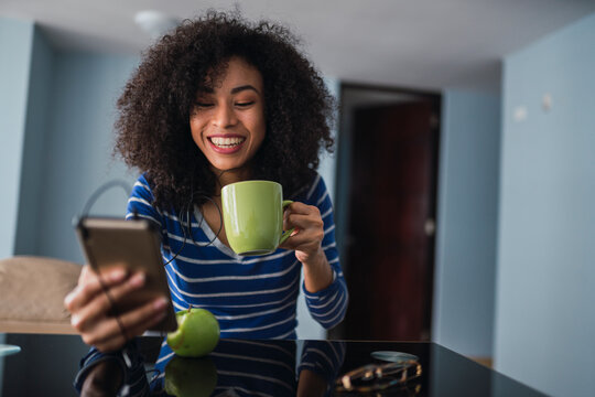 Portrait of happy young woman with coffee mug while looking at cell phone