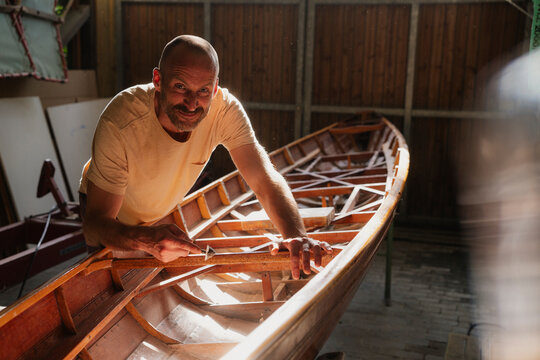 Man crafting a wooden boat in sunlight inside a tranquil workshop